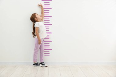 Sevimli küçük kız, boyunu beyaz duvarın yanında ölçüyor.