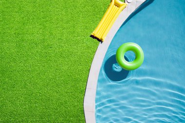 Yeşil çimlerle çevrili yüzme havuzunda yüzen şişme halka.