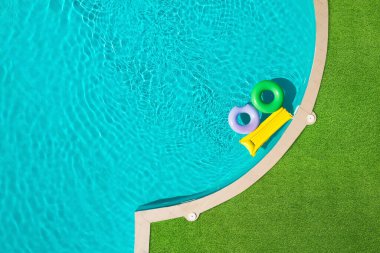 Yüzme havuzunda yüzen şişme halkalar ve şilte yeşil çimlerle çevrili.