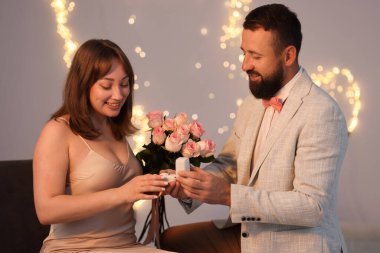 Nişan yüzüklü bir adam, açık gri arka planda, bulanık ışıklı, bokeh efektli kız arkadaşına evlenme teklif ediyor.