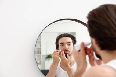 Akne sorunu olan genç bir adam evdeki aynanın yanındaki yüzüne krem sürüyor. Mesaj atmak için yer var.