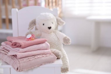 İçerideki küçük koltukta temiz bebek kıyafetleri ve aksesuarlar yığını, yakın plan. Metin için boşluk