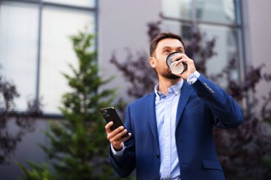Paket kahve. Kağıt bardakta içki ve açık havada akıllı telefon kullanan adam, düşük açılı görüş. Metin için boşluk