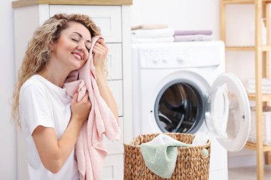 Çamaşır makinesinin yanında temiz çamaşırları olan bir kadın.