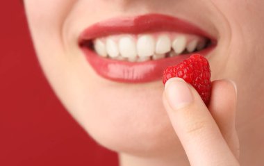 Güzel dudakları makyajlı ve kırmızı arka planda ahududu olan kadın, yakın plan.