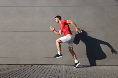 Spor giyimli bir adam binanın yanında koşuyor. Açık havada, mesaj için yer var.