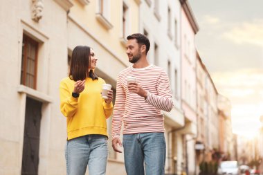 Paket kahve. Kağıt bardakta içki içen çift şehir caddesinde yürüyor, düşük açılı. Metin için boşluk