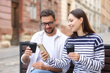 Paket kahve. Açık hava bankında kağıt bardaklar ve akıllı telefonlar olan bir çift.