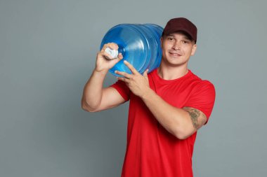 Gri arka planda soğuk su şişesiyle gülümseyen teslimatçı. Metin için boşluk