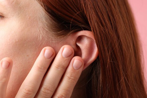 Sound. Woman touching her ear on pink background, closeup