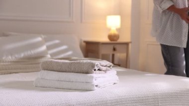 Kadın evdeki yatağa temiz havlu sepeti koyuyor, yakın plan.