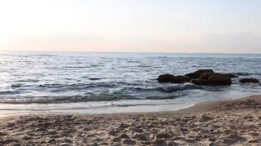 Güzel dalgalı deniz, taşlar ve kumlu sahil, sola hareket eden kamera.