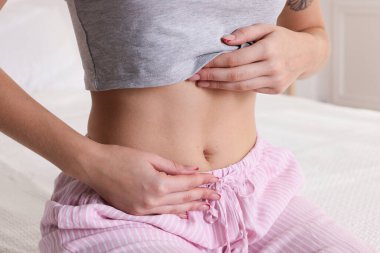 Düz göbekli genç bir kadın, yatağında, yakın plan.