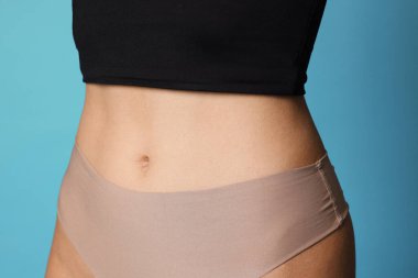 Açık mavi arka planda düz göbekli genç kadın, yakın plan.