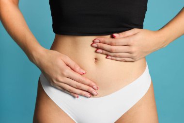 Açık mavi arka planda düz göbekli genç kadın, yakın plan.