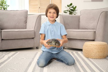 Mutlu çocuk kaplumbağasını evinde yerde tutuyor.