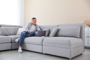 Evde kanepede dizüstü bilgisayar kullanan genç adam