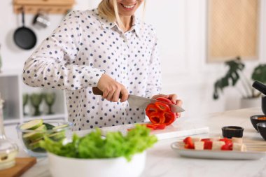 Yemek pişirme süreci. Mutfakta biber kesen gülümseyen kadın, yakın plan.