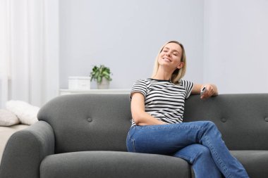 Evdeki kanepede klimalı uzaktan kumandalı bir kadın. Metin için boşluk