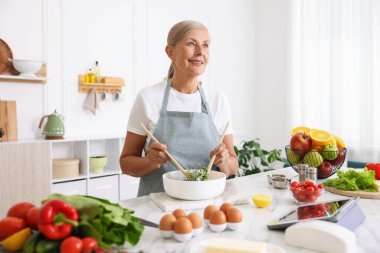 Üst düzey kadın mutfaktaki beyaz mermer masada salata pişiriyor.