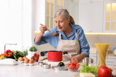 Üst düzey kadın mutfaktaki beyaz mermer masada yemek pişiriyor.