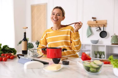 Mutfaktaki masada yemek yapan gülümseyen kadın.