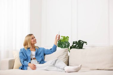 Evdeki koltukta uzaktan kumandayla klima kullanan bir kadın.