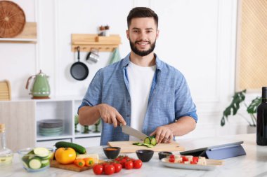 Yemek pişirme süreci. Mutfakta salatalık kesen gülümseyen adam.