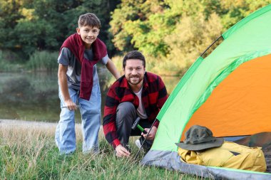 Mutlu baba ve oğul nehir kenarında kamp çadırı kuruyorlar.