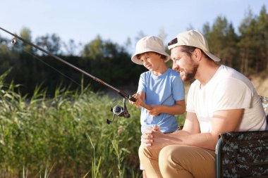 Mutlu baba ve küçük oğlu açık havada birlikte balık tutuyorlar.