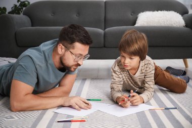 Baba ve oğul evde yerde birlikte çiziyorlar.