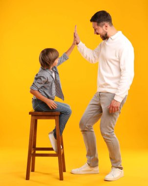 Baba oğul sarı arka planda beşlik çakıyor.