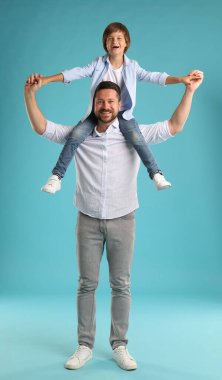 Baba oğlunu açık mavi arka planda omuzlarında taşıyor.