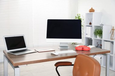 Ofisteki ahşap masada bilgisayar, dizüstü bilgisayar, tablet ve kulaklık ile modern işyeri