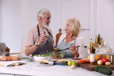 Yaşlı çift mutfaktaki masada birlikte yemek pişiriyor.