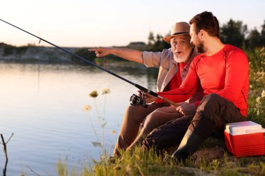Duygusal yaşlı baba ve oğlu nehir kenarında birlikte balık tutuyorlar.