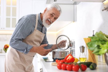 Mutfaktaki mutfağın tepesinde yaşlı bir adam yemek pişiriyor.