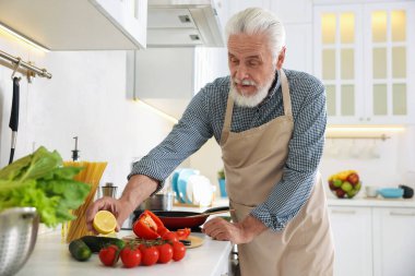 Mutfaktaki mutfağın tepesinde yaşlı bir adam yemek pişiriyor.