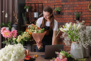 Profesyonel çiçekçi dükkandaki ahşap masada çiçek buketi yapıyor.