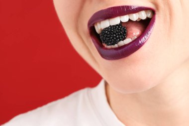 Dudak makyajı ve kırmızı arka planda böğürtlen olan güzel bir kadın, yakın plan. Metin için boşluk