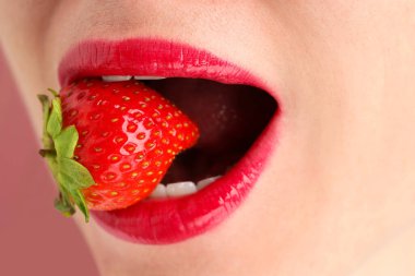 Dudak makyajı yapan güzel bir kadın ve tozlu pembe arka planda çilek, yakın plan.