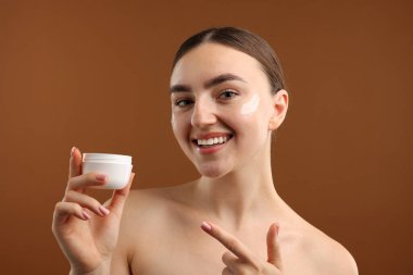 Kahverengi arka planda yüz kremi kavanozu olan güzel bir kadın.