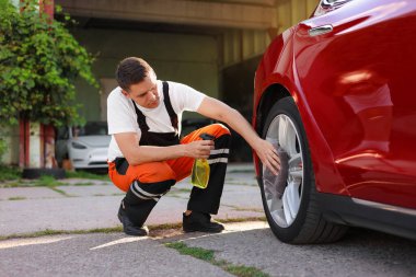 Dışarıdaki gri mikrofiber bez parçasıyla araba tekerleklerini silen adam.