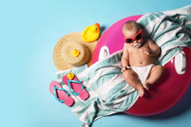 Güneş gözlüklü şirin bir bebek. Şişirilebilir yüzüğü ve açık mavi arka planda plaj aksesuarları var.