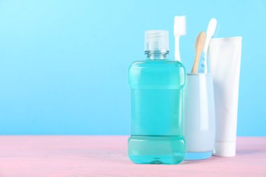 Ağız gargarası, diş macunu ve pembe ahşap masadaki diş fırçaları mavi arka planda, yazı için yer var. Ağız temizliği.