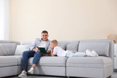 Baba ve oğlu evdeki kanepede kitap okuyorlar.