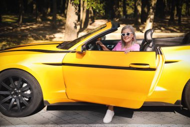 Güneş gözlüklü şık bir son sınıf öğrencisi modern Cabriolet 'ten dışarı çıkıyor.