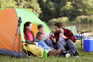Mutlu bir aile kamp çadırı, turistik malzemeler ve nehir kenarında içki molası veriyor.
