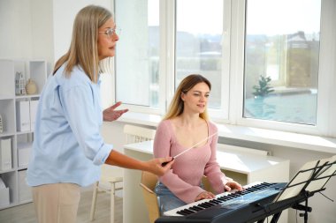 Öğretmenim kadınlara evde piyano çalmayı öğretiyor.