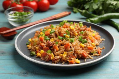 Açık mavi ahşap masada servis edilen sebzeli pilav ve domuz pastırması.